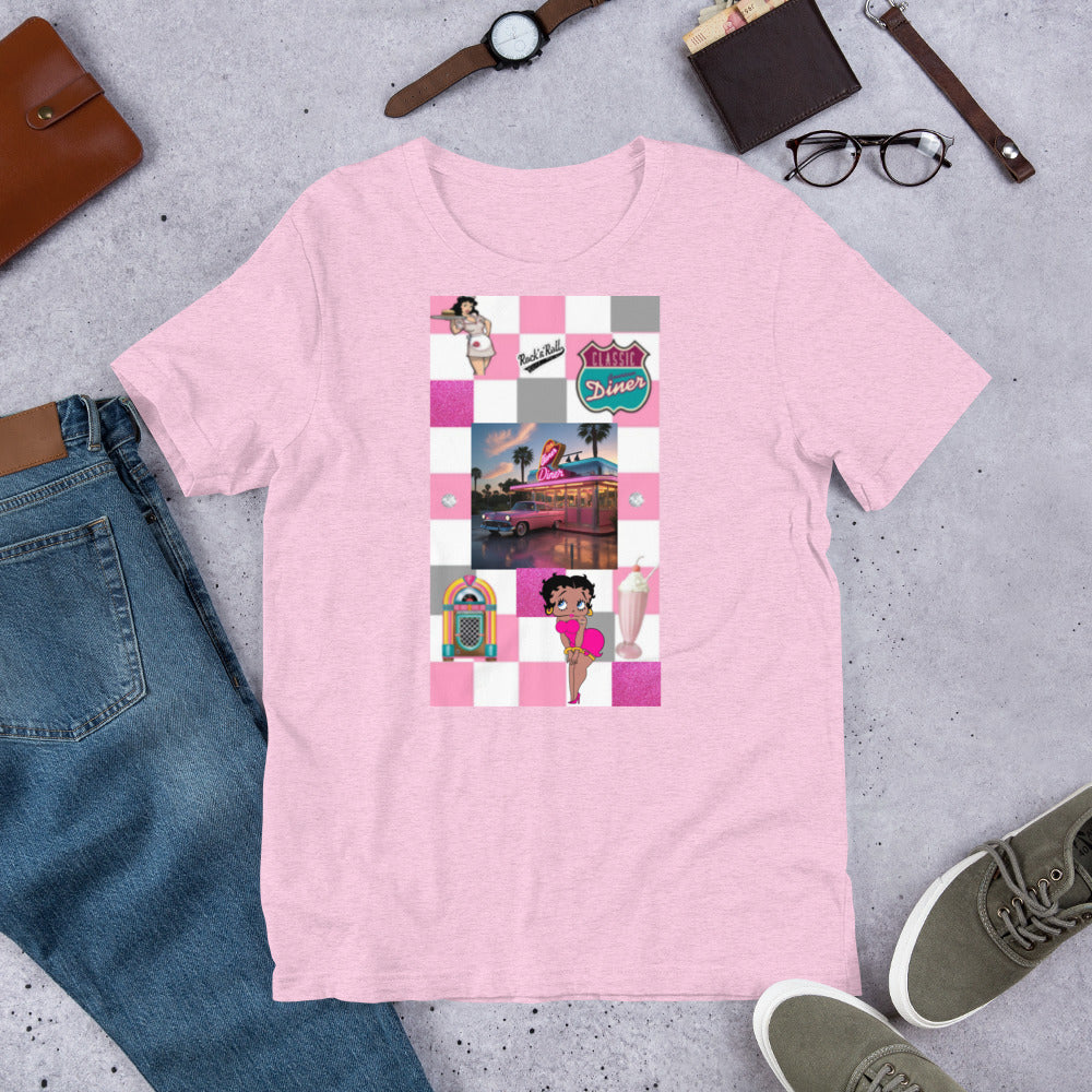 1950's pink unisex t-shirt with retro diner graphics displayed flat on a concrete background surrounded by accessories.